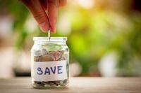 A hand drops coins into a glass jar labeled &quot;save&quot;